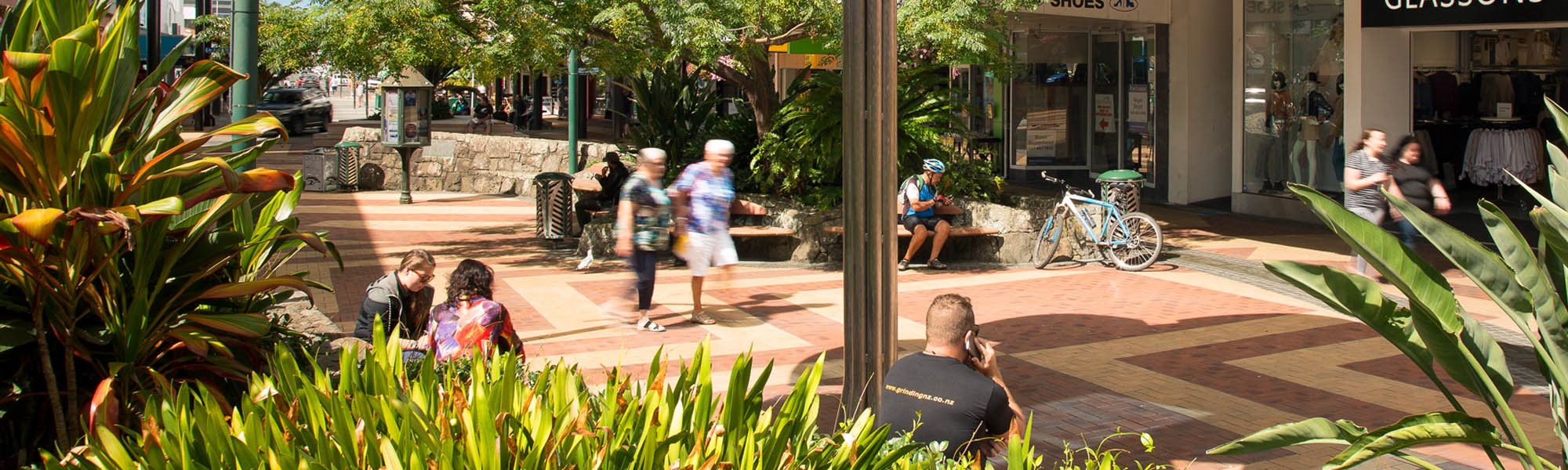 People sitting in the Cameron Street paved area of the main Whangārei shopping centre, with lovely gardens around them. 