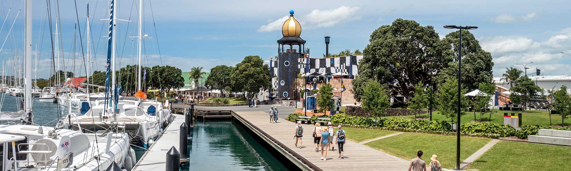 An image of the Town Basin in Whangarei, with Hundertwasser Art Centre in the background and people walking along the waterfront